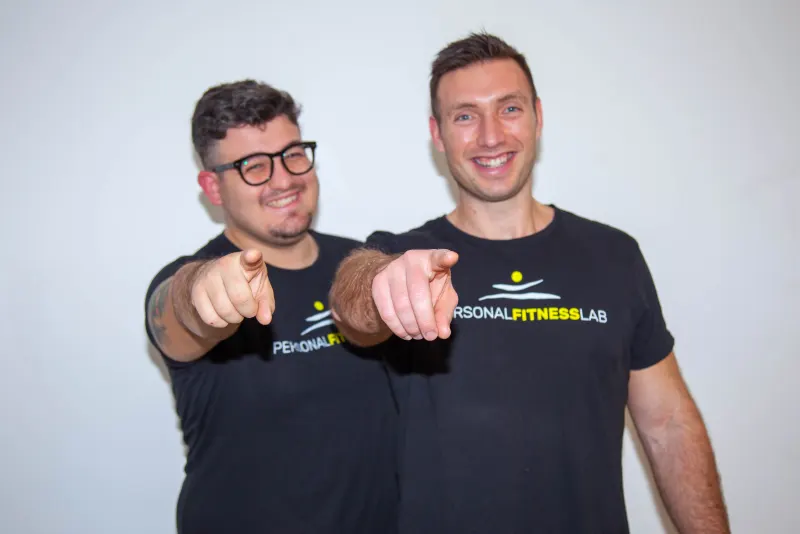 I due trainer di Personal Fitness Lab sorridono indicando l'obiettivo.